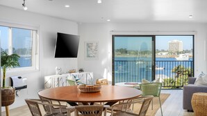 Een moderne woonkamer met een eetgedeelte, grote ramen, een flatscreen televisie en uitzicht op zee.
