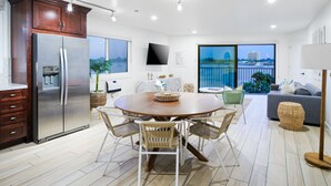 Een moderne keuken met een grote koelkast, een eettafel met stoelen en een uitzicht op de stad door grote ramen.