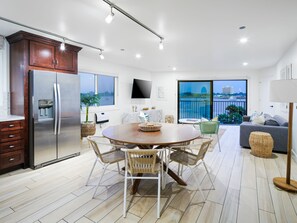 Une cuisine moderne dotée d’un grand réfrigérateur, d’une table à manger avec des chaises, et offrant une vue sur la ville grâce à de grandes fenêtres.