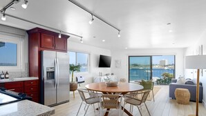 Een moderne keuken met een groot eiland, een eethoek met rieten stoelen en een balkon met uitzicht op zee.