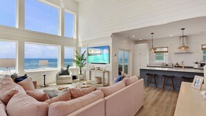 A spacious living area with a large window overlooking the ocean, a comfortable seating area, and a modern kitchen with bar stools.