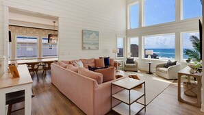 A spacious living room with a large pink sofa, a coffee table, and a view of the ocean through large windows.