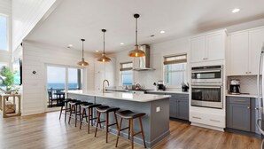 A modern kitchen with a large island, bar stools, stainless steel appliances, and a view to the ocean.
