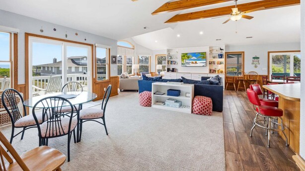 A spacious living area with a large sofa, a dining table, and chairs. There is a balcony with a view of the ocean. - Fore Decs: Private Pool, Tiki Bar & Ocean Views (Corolla)