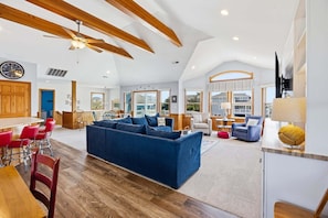 A spacious living area with a large blue sofa, wooden ceiling beams, and a dining area with red chairs.