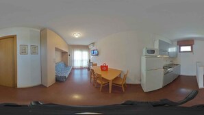 A compact living space with a kitchenette, a dining area with a table and chairs, a sofa, and a television.