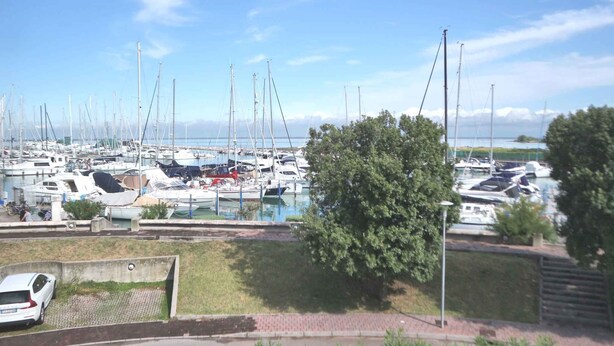 A marina with numerous boats docked, a grassy area, and a paved walkway. - Holiday apartment mit Klimaanlage und Balkon (Lignano Sabbiadoro)