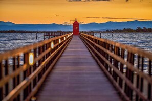 Une jetée en bois mène à une structure de phare rouge, d’où l’on a une vue dégagée sur les montagnes en arrière-plan.
