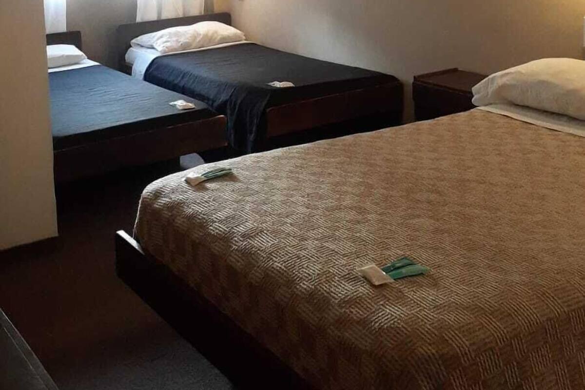 A hotel room with two single beds, a large bed, a ceiling fan, and a window with curtains.