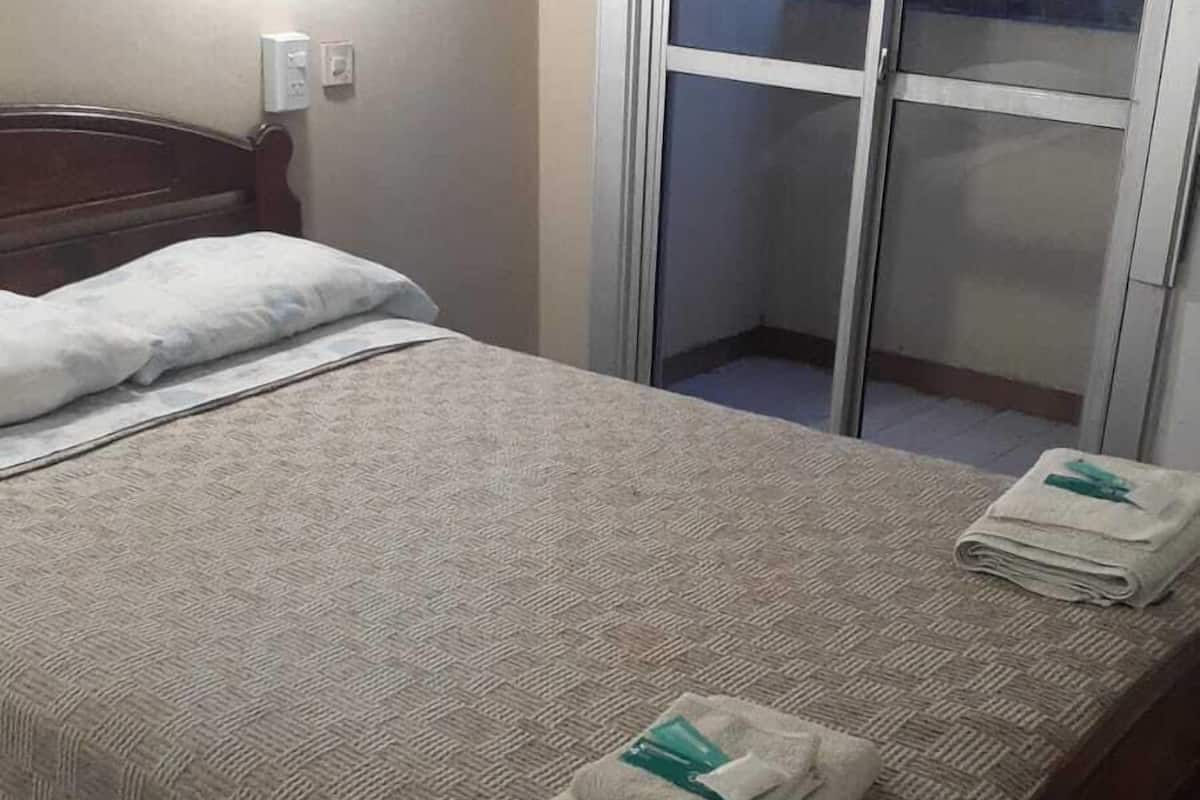 A neatly made bed with a patterned bedspread and folded towels on the side.