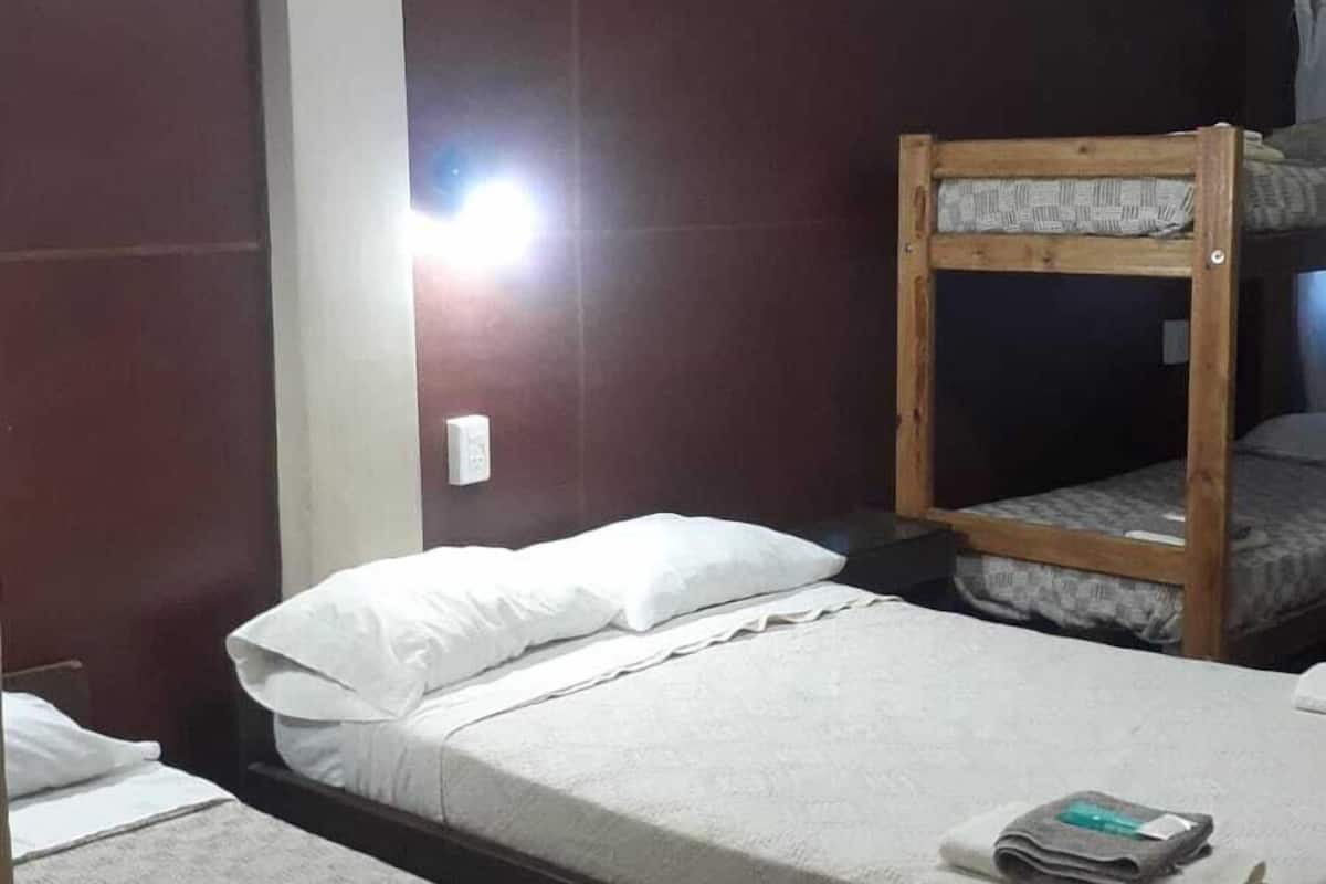 A hotel room with two single beds, a ceiling fan, and a wooden bunk bed.