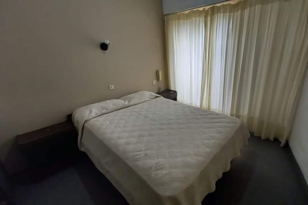 A hotel room with a single bed, a bedside table, a telephone, and a curtain.
