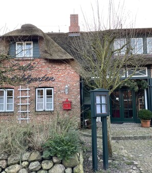 A traditional brick building with a thatched roof, a sign reading "The Blacksmith," and a stone wall in the foreground.