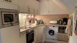 A compact kitchen with a microwave, oven, washing machine, and a small sink. - Ferienwohnung Apfelrose - Urlaub im Malerischen Inseldorf Oldsum (Oldsum)