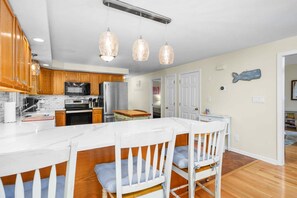 Una cocina con armarios de madera, un refrigerador de acero inoxidable y una encimera blanca. Hay tres lámparas colgantes sobre la encimera.