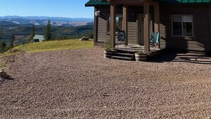 Une cabane en bois avec un toit vert, une véranda dotée de deux chaises et une allée gravillonnée.