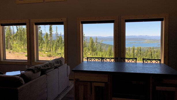 Une pièce dotée d’une grande table à manger, d’une banquette intégrée et de nombreuses fenêtres donnant sur une forêt et un lac.