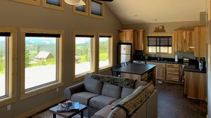 Un vaste espace de vie comprenant un canapé, une table à manger et un ventilateur de plafond. De grandes fenêtres offrent une vue sur un paysage montagneux.