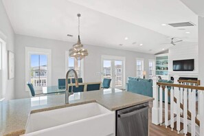 Een moderne keuken met een ingebouwde vaatwasser, een eethoek met een glazen tafel, en een woonkamer met een televisie en zitplaatsen.