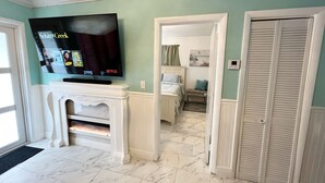 Ein Wohnzimmer mit Kamin, einem an der Wand befestigten Fernseher und einem Flur, der zum Schlafzimmer führt.
