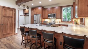 Una cocina con armarios de madera, un refrigerador de acero inoxidable, un microondas y una isla grande con taburetes de bar.
