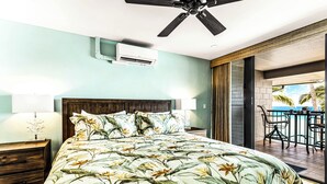 Un dormitorio con una cama grande, un equipo de aire acondicionado, un ventilador de techo y vistas a una piscina y palmeras.