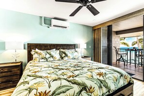 Une chambre dotée d’un grand lit, d’un climatiseur, d’un ventilateur de plafond et offrant une vue sur une piscine et des palmiers.