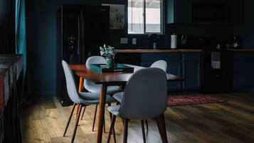 A modern kitchen with a dining area, wooden flooring, and a view through a window.