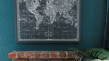 Un mapa mundial enmarcado sobre una pared verde azulada, encima de una chimenea de ladrillo.