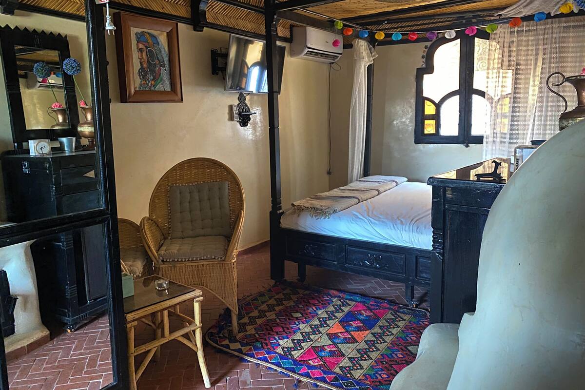 Quarto tradicional com cama, cadeira, mesinha e espelho.