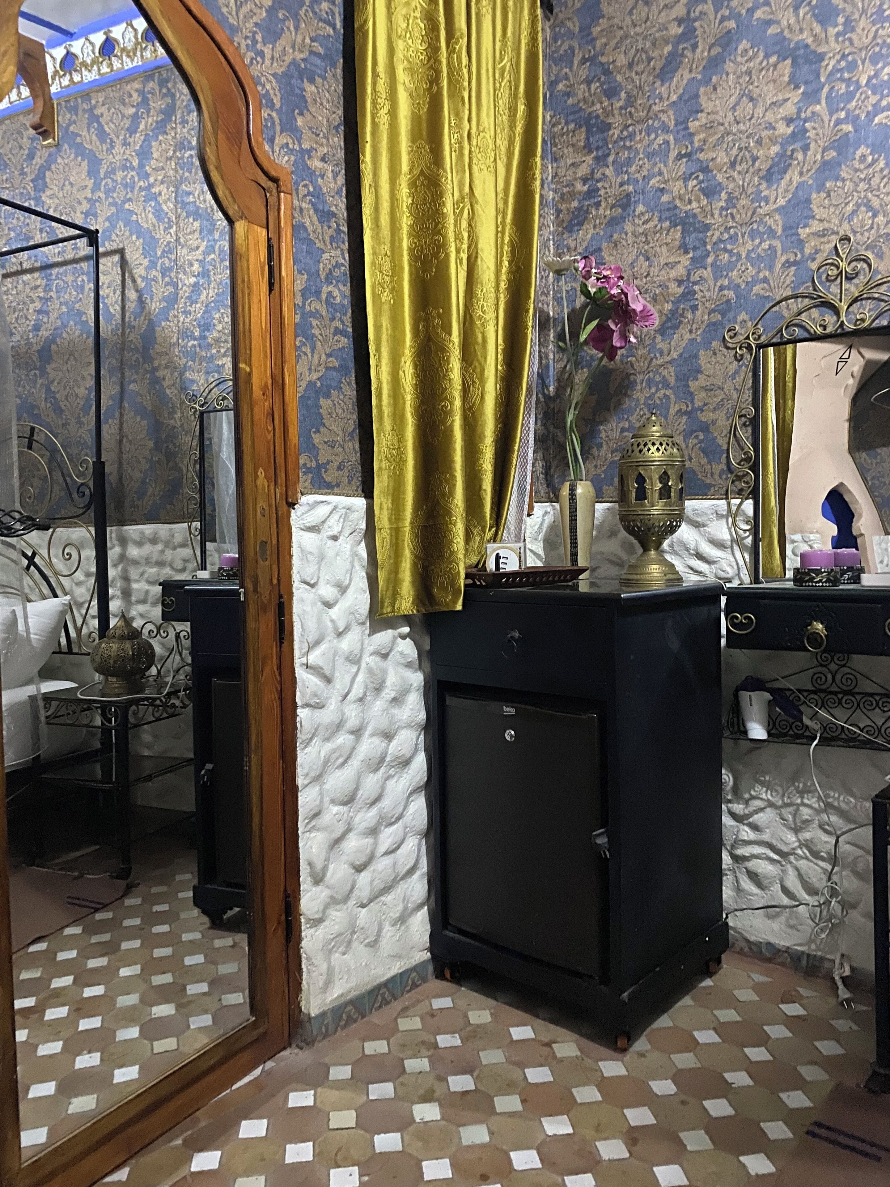 Un baño con un lavabo negro, un espejo, una lámpara decorativa y un papel tapiz estampado.