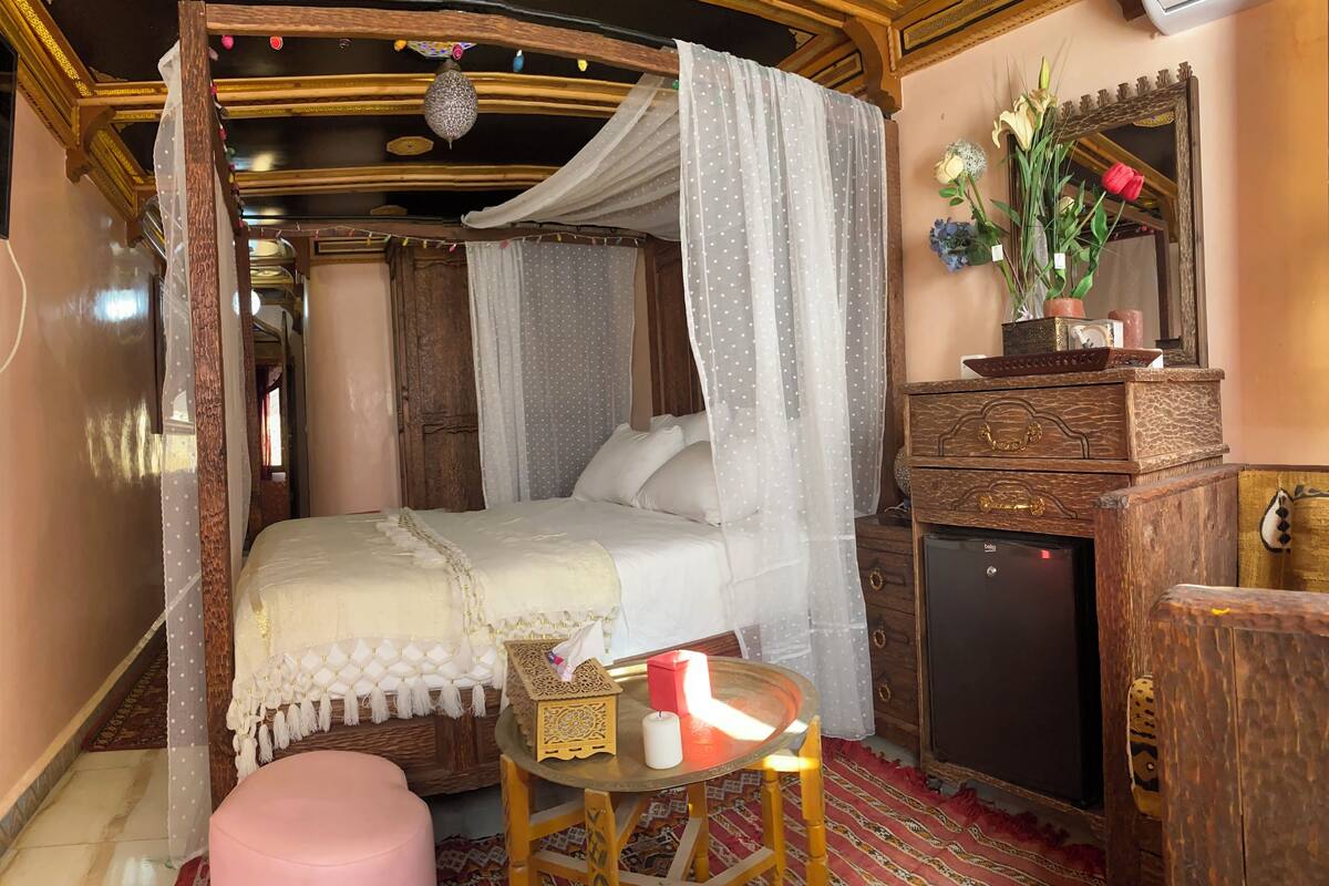 Quarto com cama de dossel, uma mesinha com uma vela e um espelho na parede.