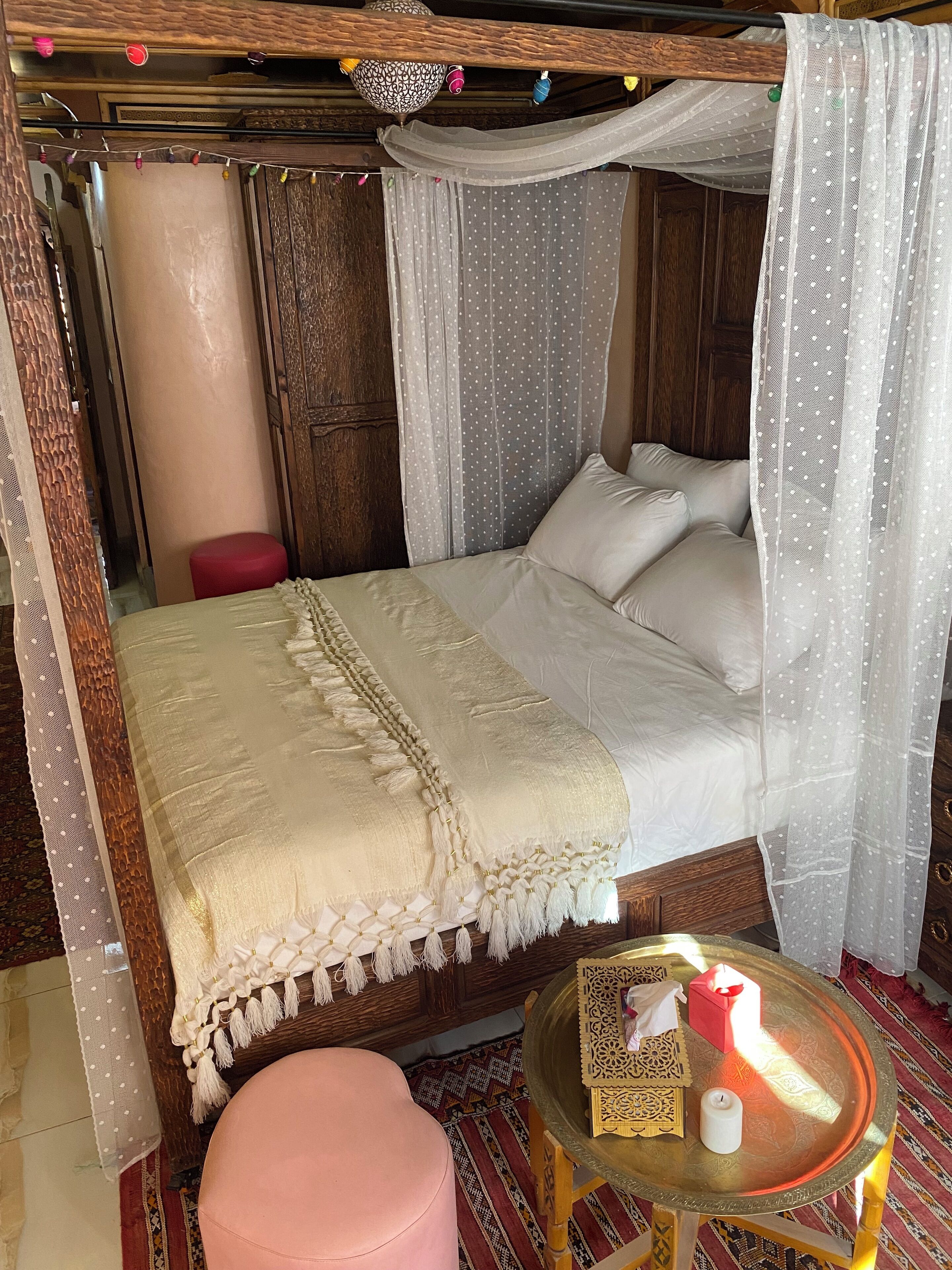 A bed with a canopy, a small table with a candle, and a red stool.