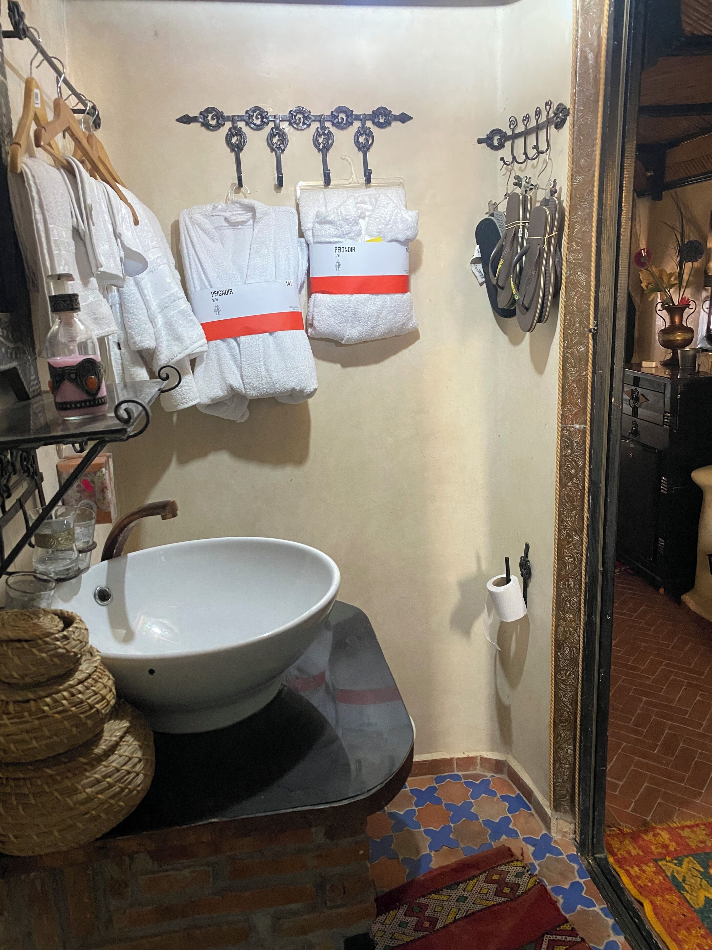 A bathroom with a white sink, hanging towels, and a decorative metal rack.