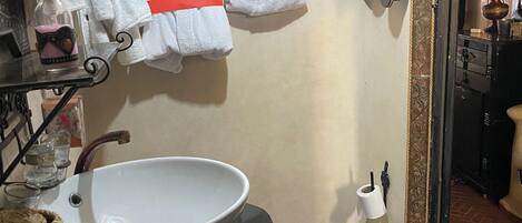 A bathroom with a white sink, hanging towels, and a decorative metal rack.
