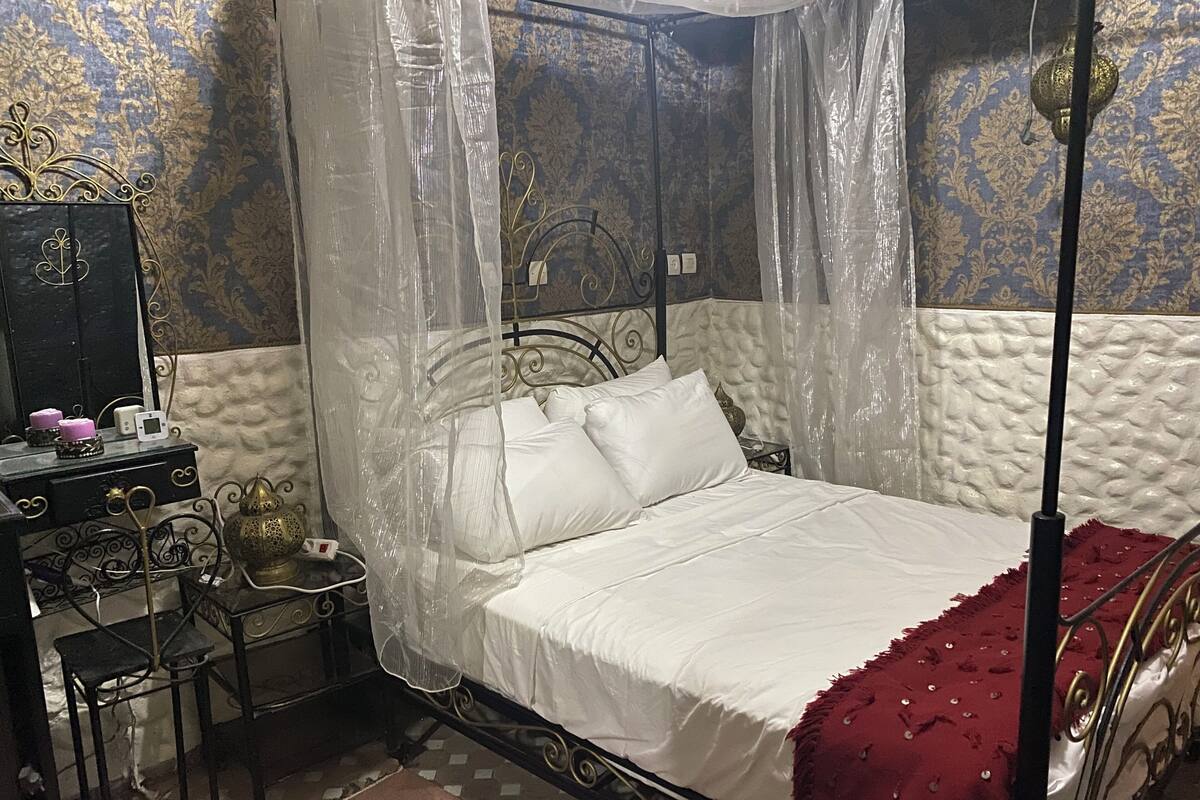 Quarto com cama, mesa de cabeceira, cadeira e luminária decorativa.