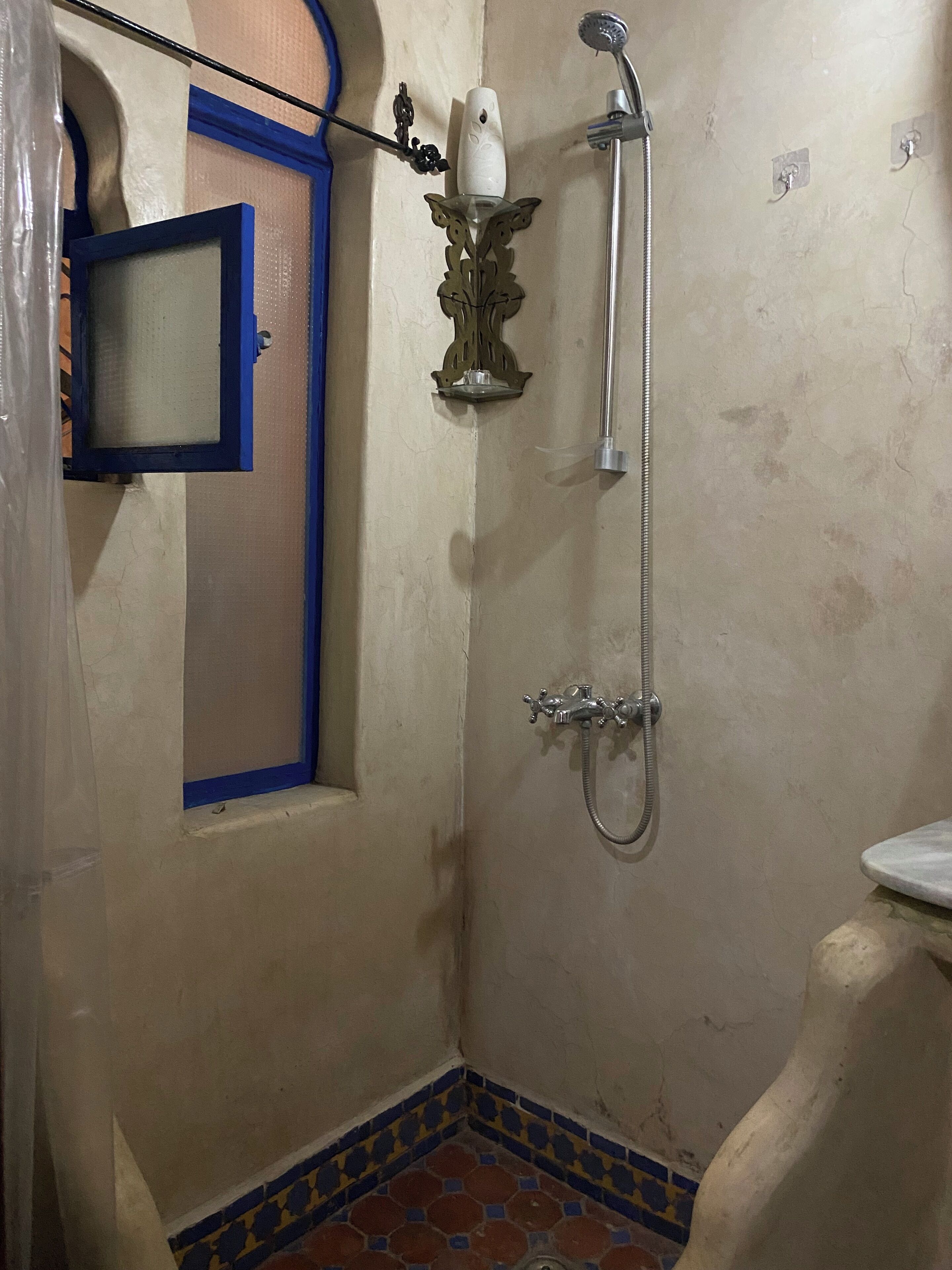 Une petite salle de bain avec une douche, des toilettes et une fenêtre dotée d’un cadre bleu.