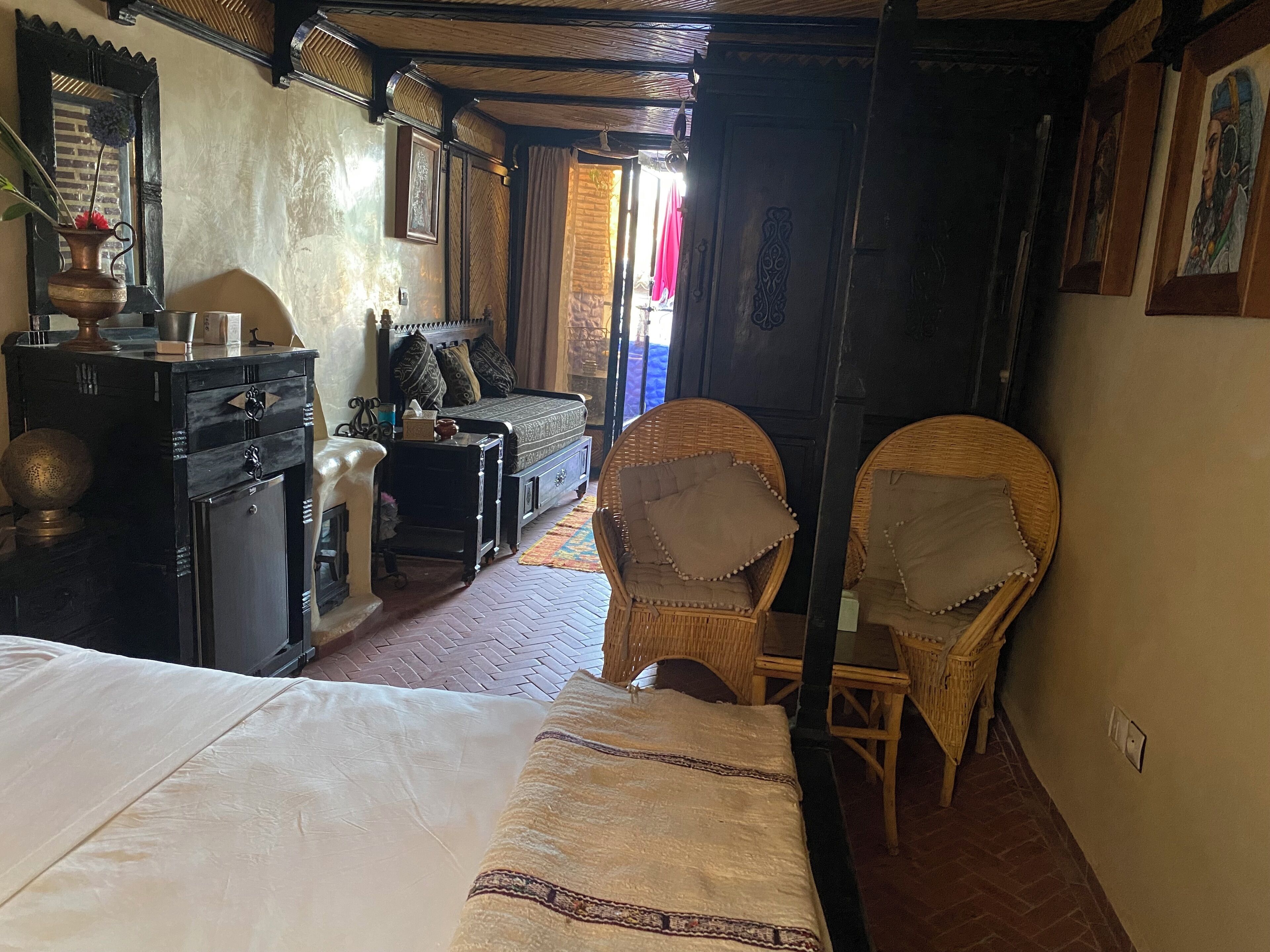 Une chambre de style traditionnel, comprenant un lit, deux fauteuils en osier, une petite table et un buffet.
