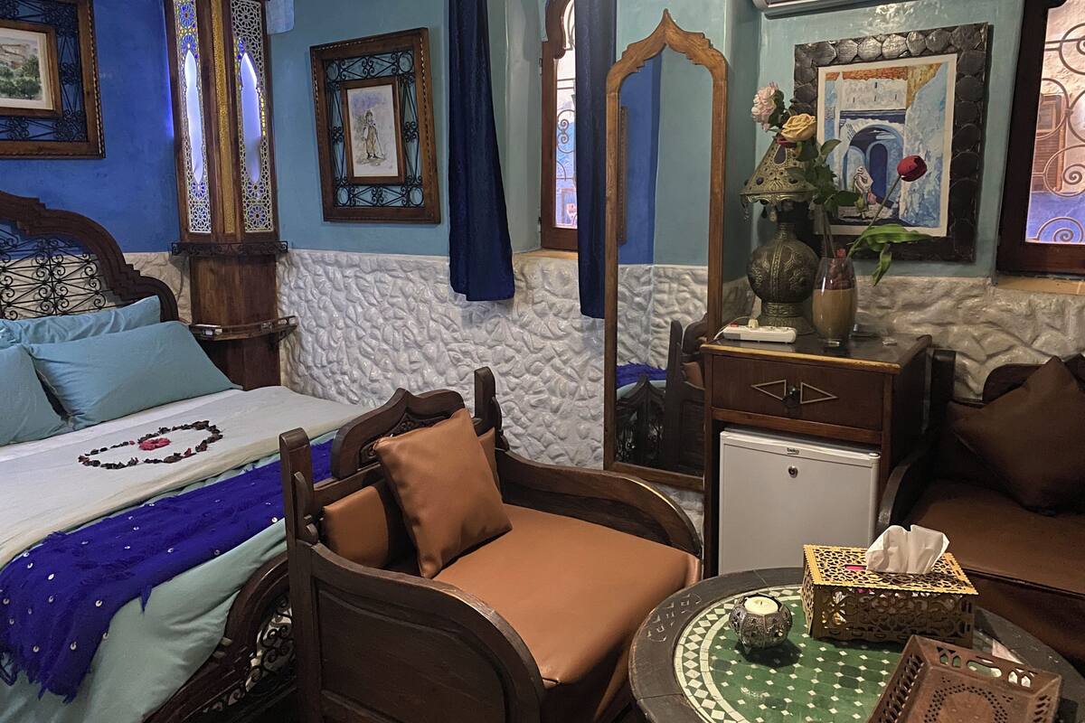 Quarto com cama, cadeira, mesa pequena e cômoda.