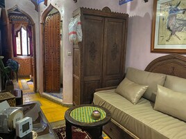 Una habitación tradicional con un sofá, un armario de madera, una mesa decorativa y una alfombra estampada.