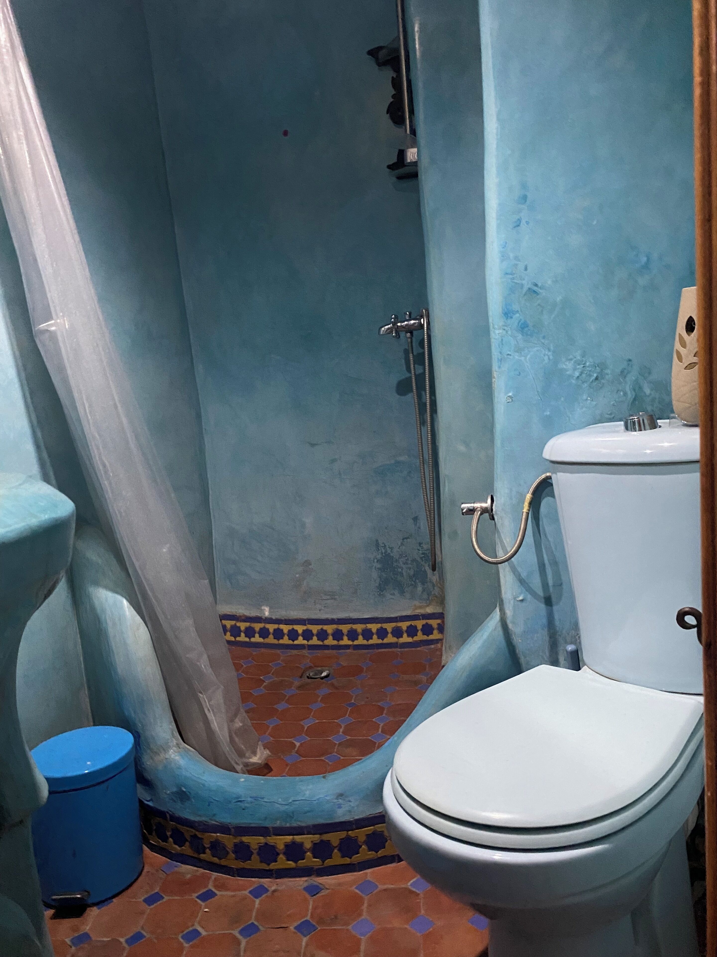 A bathroom with a shower, toilet, and blue-tiled floor.