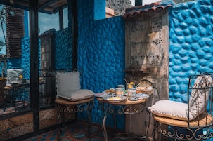 A cozy outdoor seating area with two metal chairs and a small round table, set against a vibrant blue textured wall.