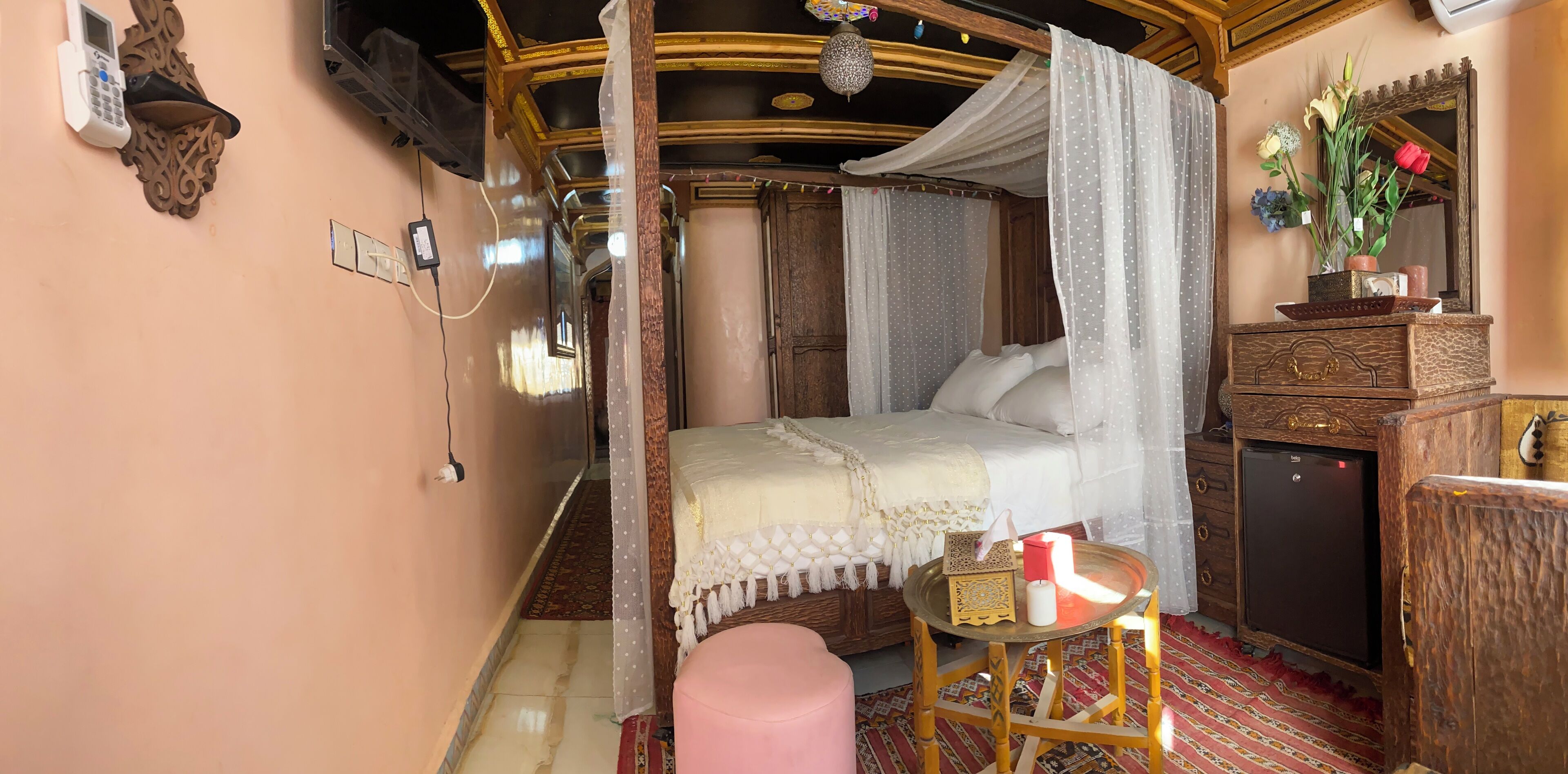 A room with a four-poster bed, a small table with a candle, a wooden cabinet, and a mirror.