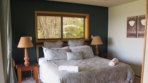 Un lit bien fait, recouvert d’une couvre-lit à motifs, avec deux lampes de chevet et une fenêtre équipée de stores.