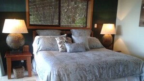 Un lit bien fait, recouvert d’une couvre-lit à motifs et agrémenté d’oreillers, flanqué de deux tables de chevet avec des lampes, d’un panier en osier et d’un tapis à motifs posé sur un sol carrelé.