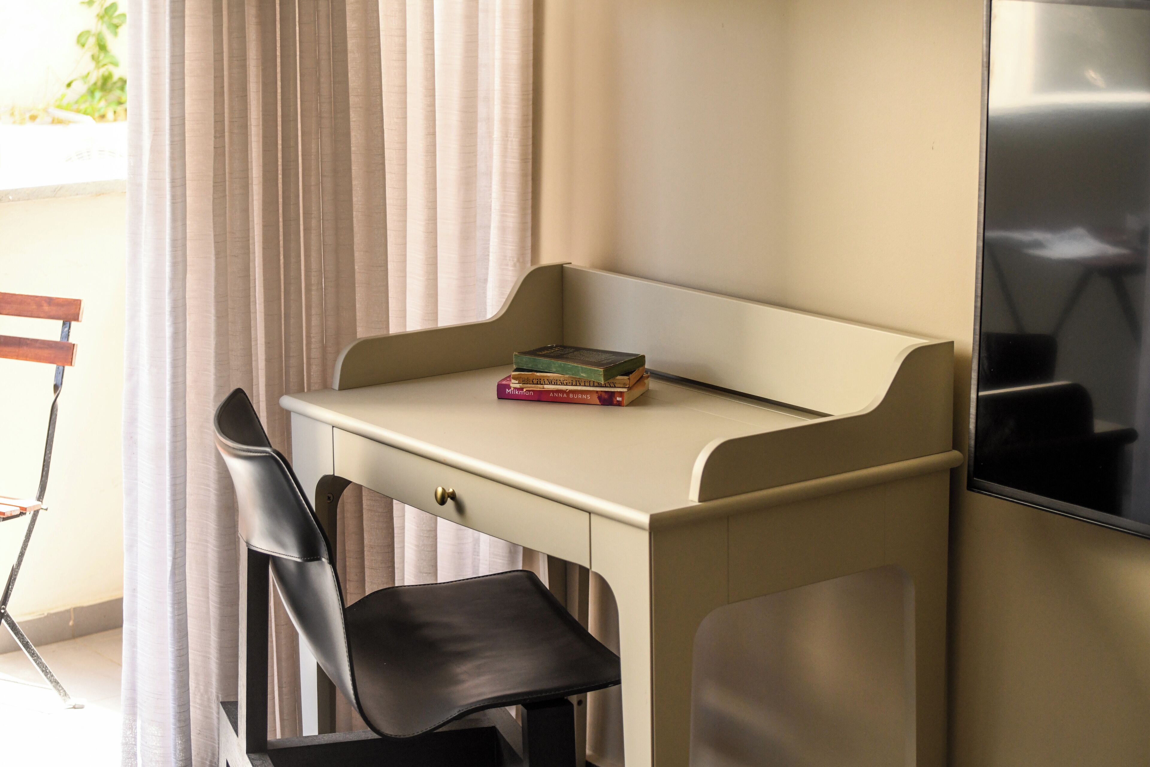 A small desk with a chair, a television, and a window with curtains.