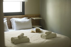 A neatly made bed with white linens, a book, and rolled towels. - White Blossom Dizengoff CTR by SeaN'Rent (Tel Aviv)