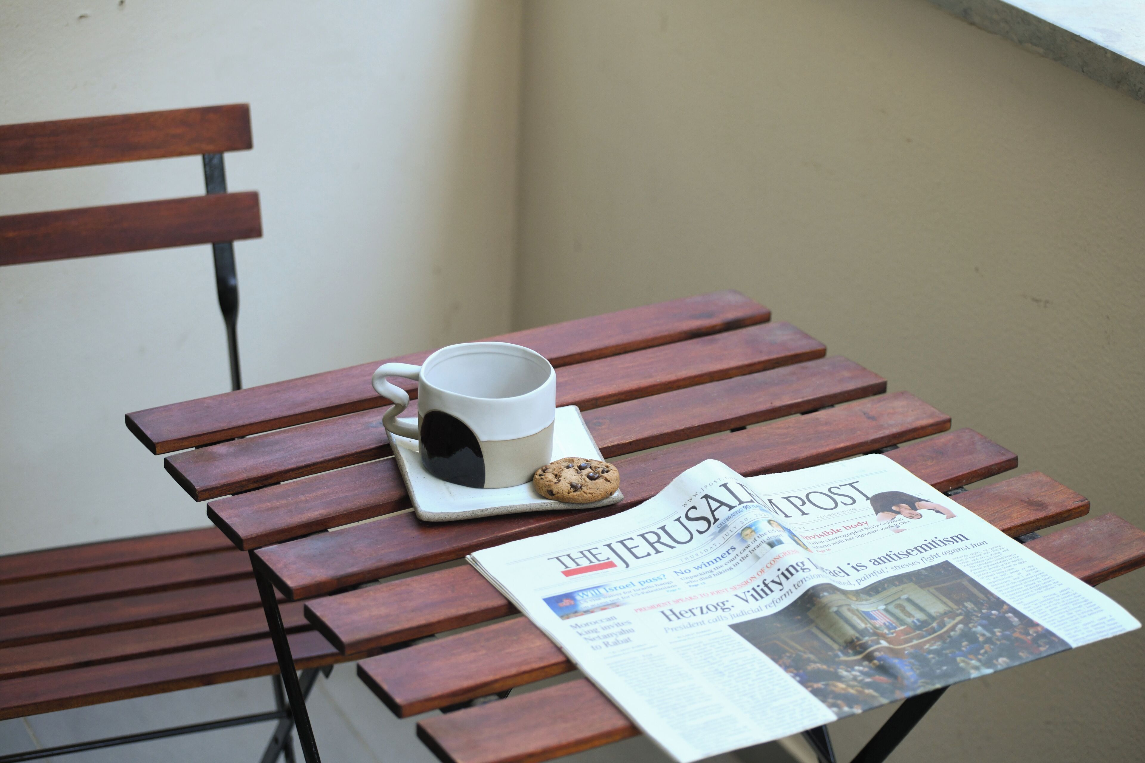 A wooden bench with a newspaper, a mug, and a cookie.