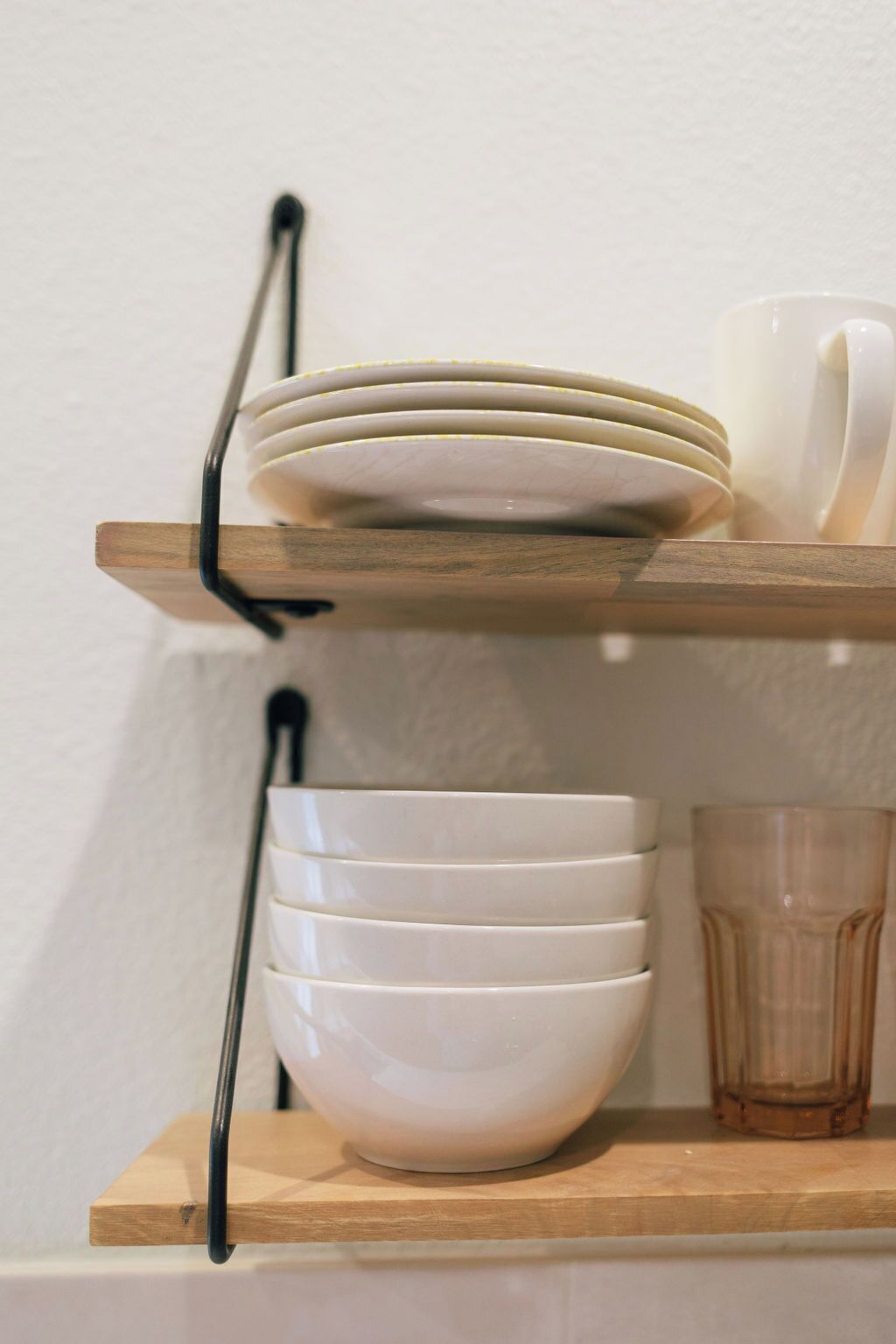 Een plank met gestapelde witte borden en kommen, een helder glazen glas, en een houten plank.