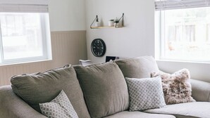 Een moderne woonkamer met een grijze modulaire bank, een sierkussen met patroon, een zacht kussen en een kleine wandklok.
